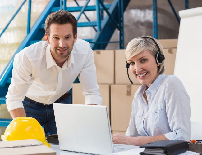 Warehouse managers using laptop and wearing headset in